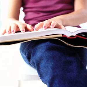 close-up of a girls hand reading Braille from a book